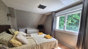 Un lit bien fait, avec des oreillers et une couverture, une table de chevet avec une lampe, et une fenêtre donnant sur un paysage verdoyant.