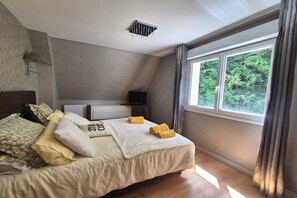 Ein ordentlich bezogenes Bett mit Kissen und Decke, ein Nachttisch mit Lampe und ein Fenster mit Blick ins Grüne.