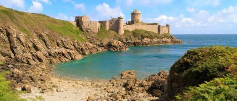 Un castillo costero con estructura fortificada, costa rocosa y aguas turquesas cristalinas.