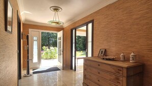 Un couloir avec un mur en bois, une porte vitrée donnant sur l’extérieur et une commode en bois ornée d’objets décoratifs.