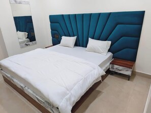 A bed with a blue upholstered headboard, white bedding, and a wooden nightstand with a marble-patterned drawer. - Hotel CS Inn & Restaurant (Agra)