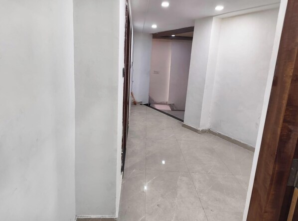 A hallway with a tiled floor, white walls, and a wooden door frame. - Hotel CS Inn & Restaurant (Agra)