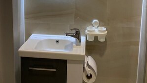 Et badeværelse med et rundt spejl, en vask, en bruseniche og en toiletpapirholder.