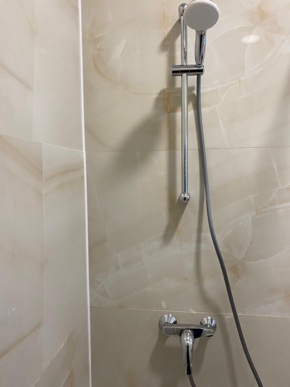A shower with a handheld showerhead and a fixed showerhead, both mounted on a wall with a tiled surface.
