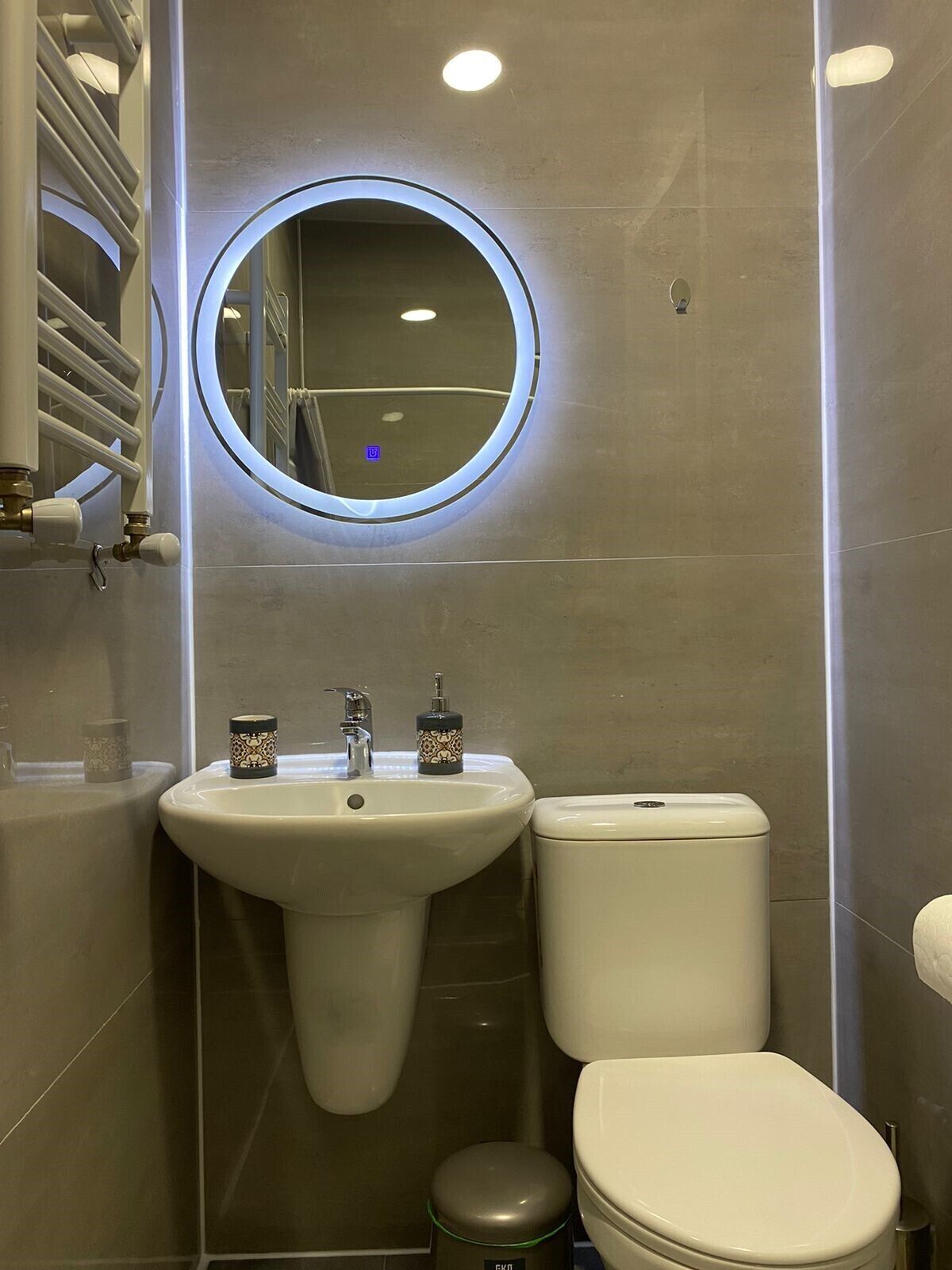 Un baño con un espejo redondo, un lavamanos y un inodoro.