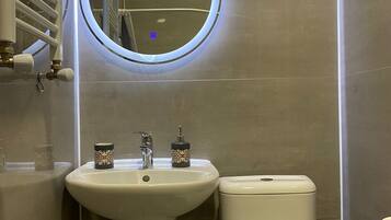 Un baño con un espejo redondo, un lavamanos y un inodoro.