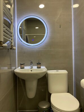 A bathroom with a round mirror, a sink, and a toilet. - Cultural Crossing Hotel (Tbilisi)
