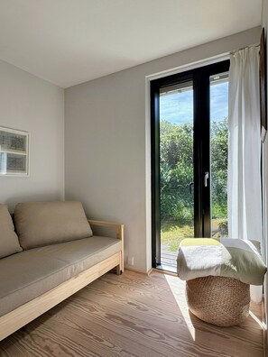 A room with a sofa, a small table, and a view through a glass door. - Terrace with a sea peek, 500 meters from the beach (ordrup)