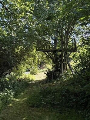 A wooden structure with a ladder, surrounded by dense foliage and a grassy path. - Terrace with a sea peek, 500 meters from the beach (ordrup)