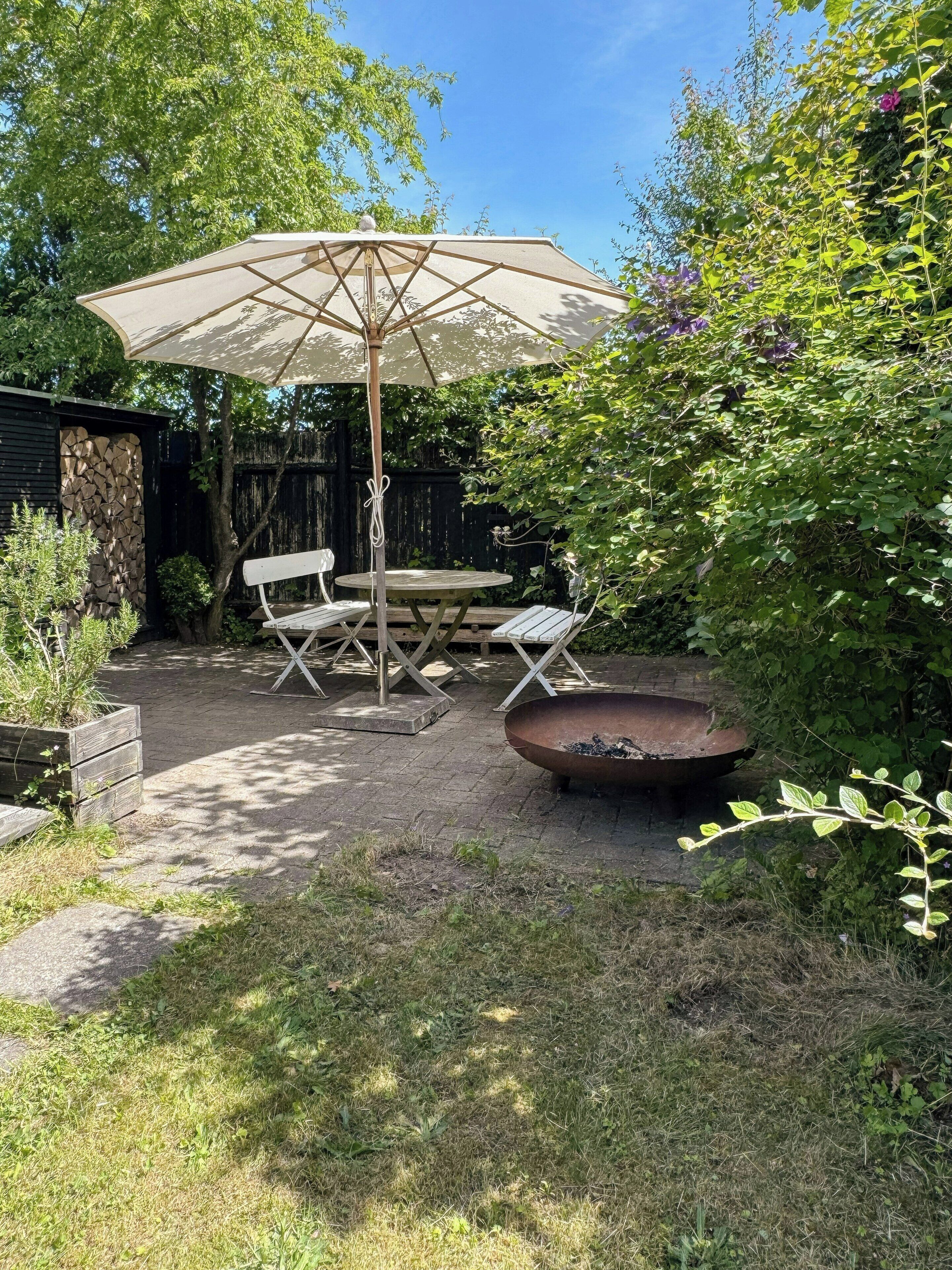A patio with a table and chairs, an umbrella, and a fire pit.
