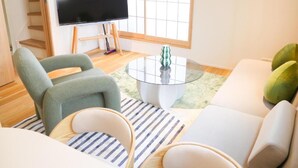 A living room with a flat-screen TV on a stand, a sofa, a chair, and a coffee table. - MSTAY Kamata Honcho (Ota-ku)
