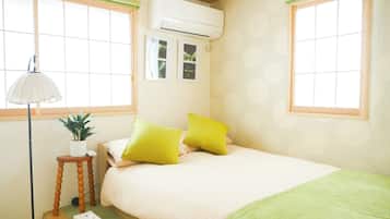 A bedroom with a bed, a bedside lamp, a small table with a plant, and a wall-mounted air conditioner.