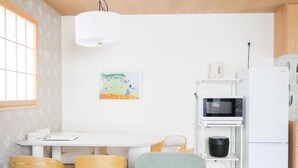 A compact kitchen with a white refrigerator, a microwave, and a dining area with wooden chairs and a white table. - MSTAY Kamata Honcho (Ota-ku)