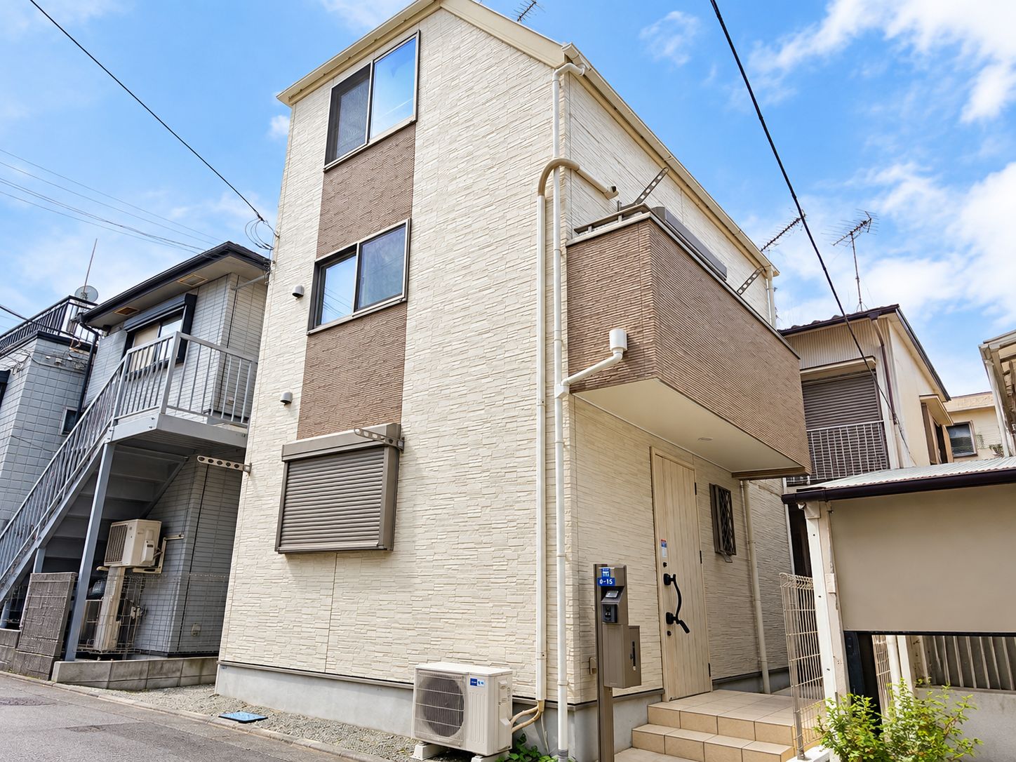 A two-story residential building with a flat roof, a small front porch, and a visible air conditioning unit.