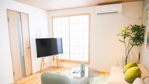 A living room with a flat-screen TV on a stand, a sofa, a coffee table, and a plant. - MSTAY Kamata Honcho (Ota-ku)