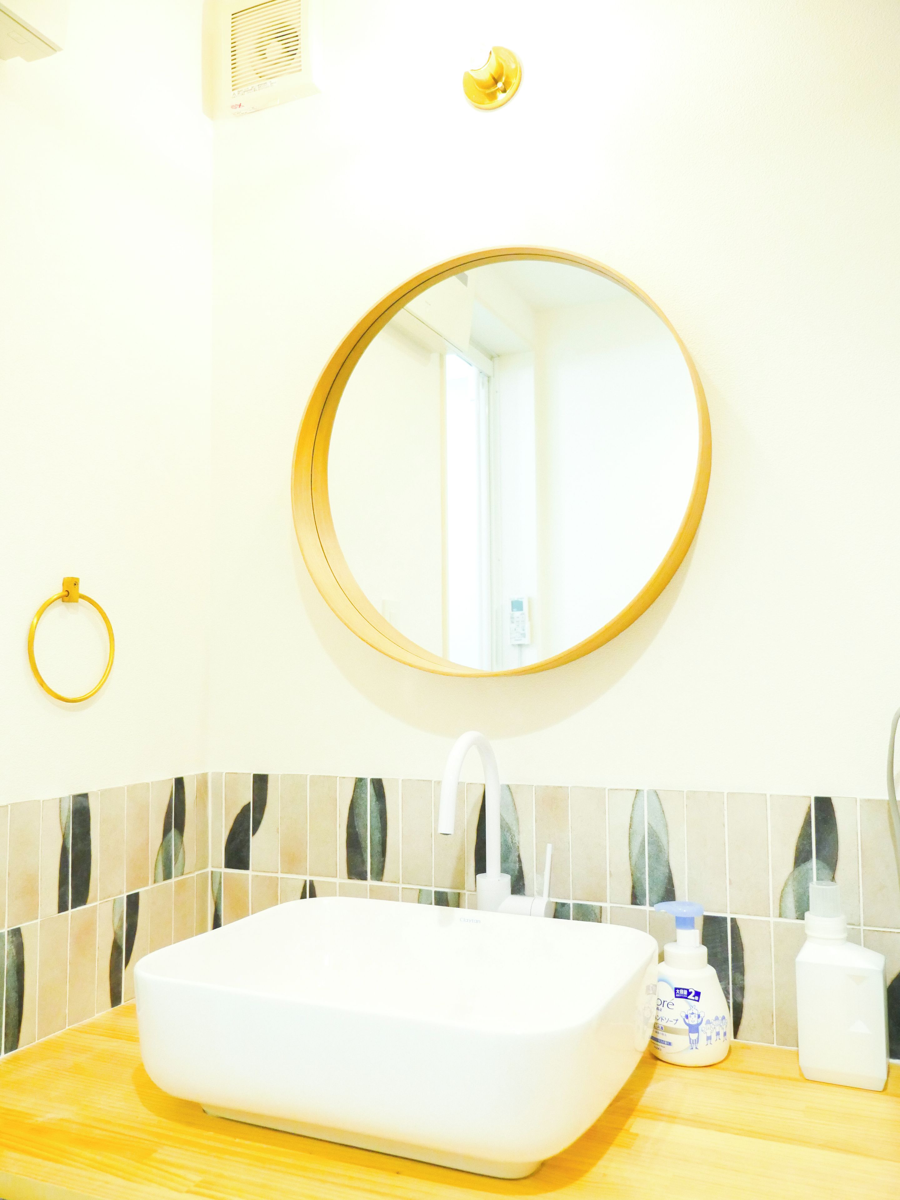 A bathroom with a white sink, a round mirror with a gold frame, and a towel ring on the wall.