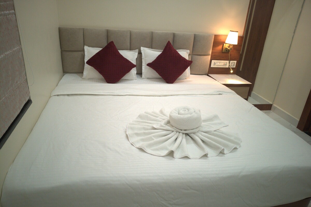 A hotel room with a neatly made bed, two pillows, a bedside lamp, and a towel arranged on the bed.