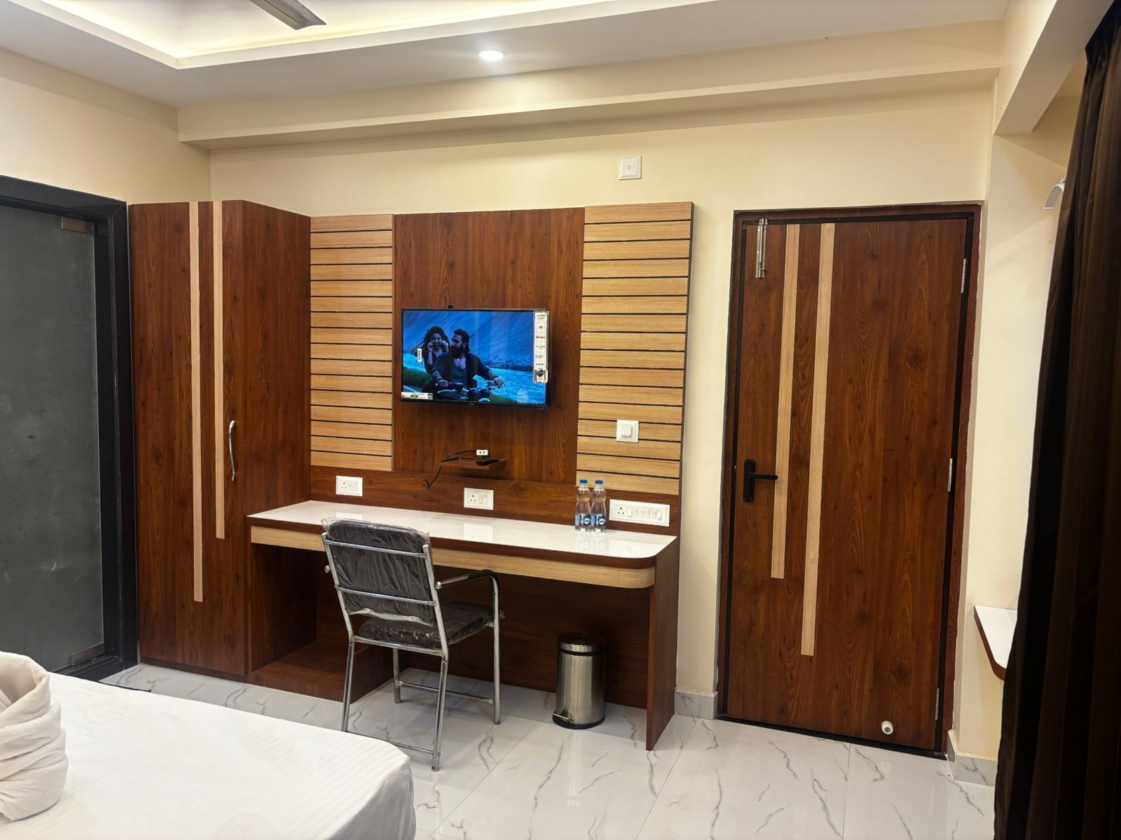 Habitación de hotel con escritorio de madera, televisor montado en la pared, cama y armario.