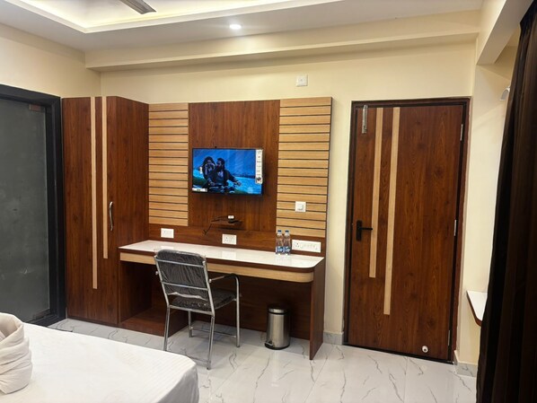 A hotel room with a wooden desk, a television mounted on the wall, a bed, and a wardrobe.