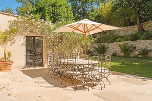 An outdoor patio with a round table and chairs, an umbrella, and a stone wall. - Luxe: Villa Ocean Whisper 8BR/16P (Saint-Tropez)