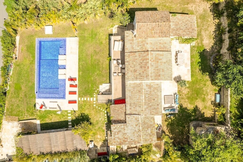 Vista aérea de uma propriedade com piscina, área de varanda e um edifício grande com telhado cerâmico.
