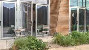 A modern building with glass doors marked with numbers 79 and 81, a wooden facade, and outdoor seating with chairs and tables. - Beautiful apartment in Aarhus C with WiFi (Aarhus C)