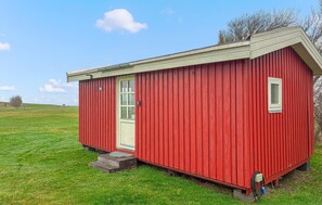 A red wooden building with a door and window, situated on a grassy field. - Stunning home in Samsø with house sea view (Samsø)