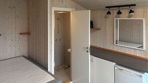 Een kleine kamer met een bed, een douche, een wastafel en een spiegel.