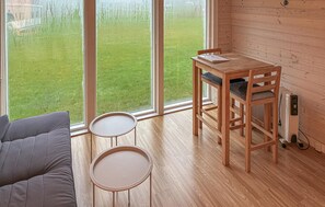 A room with a wooden table and chairs, a small round table, a sofa, and a view of a green lawn through large windows. - Gorgeous home in Samsø with house sea view (Samsø)