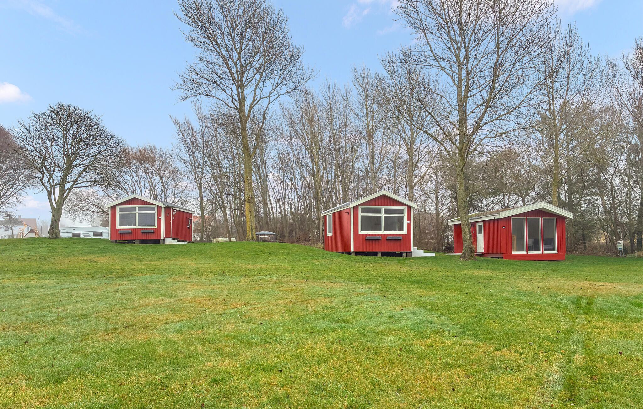 Three red cabins with large windows, set in a grassy field with trees in the background.