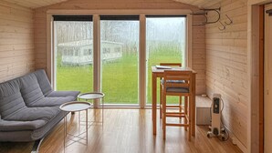 Ein gemütliches Zimmer mit einer Couch, einem kleinen Tisch und einem Stuhl. Große Fenster bieten Blick auf eine Rasenfläche.