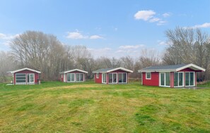 Trois mobil-homes rouges, dotés de grandes fenêtres, se dressent devant un champ verdoyant.