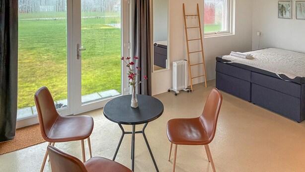 Une chambre avec un lit, un radiateur, une table avec des chaises et une vue sur un espace extérieur verdoyant.