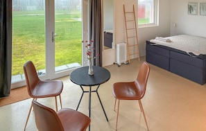 Ein Zimmer mit einem Bett, einem Heizkörper, einem Tisch mit Stühlen und Blick auf eine grüne Außenanlage.