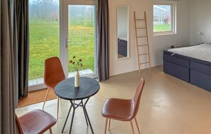 Ein Zimmer mit einem Bett, einem Tisch mit Stühlen, einer Vase mit Blumen und Blick auf eine grüne Landschaft durch das Fenster.