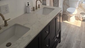 Un baño con tocador de mármol, dos lavamanos, un espejo grande y un inodoro.