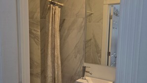 Un baño con ducha, lavamanos y espejo.