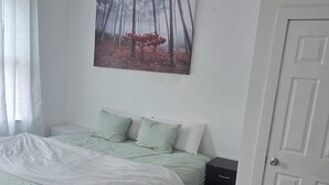 Un dormitorio con cama, un cuadro, una puerta y una ventana con cortinas.