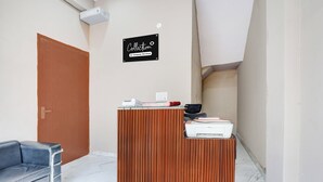 A reception desk with a sign above it, a wooden door, a black office chair, and a white marble floor. - Collection O Sector 33 Gurgaon (Gurugram)