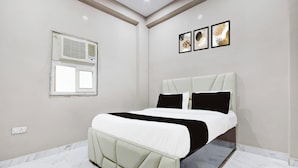 A bedroom with a bed, a window with an air conditioner, and three framed pictures on the wall. - Collection O Sector 33 Gurgaon (Gurugram)