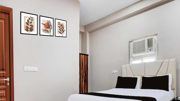 A bedroom with a bed, a window with blinds, a door, and three framed pictures on the wall. - Collection O Sector 33 Gurgaon (Gurugram)