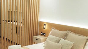 Une chambre d’hôtel comprenant un lit, des oreillers, une table de chevet, une cloison en bois et un luminaire fixé au mur.