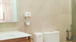 Une salle de bain comprenant des toilettes, un distributeur de savon liquide, une douche et un meuble-lavabo en bois.