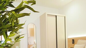 Une chambre d’hôtel avec un lit, un miroir, une armoire, une table de chevet et une plante en pot.