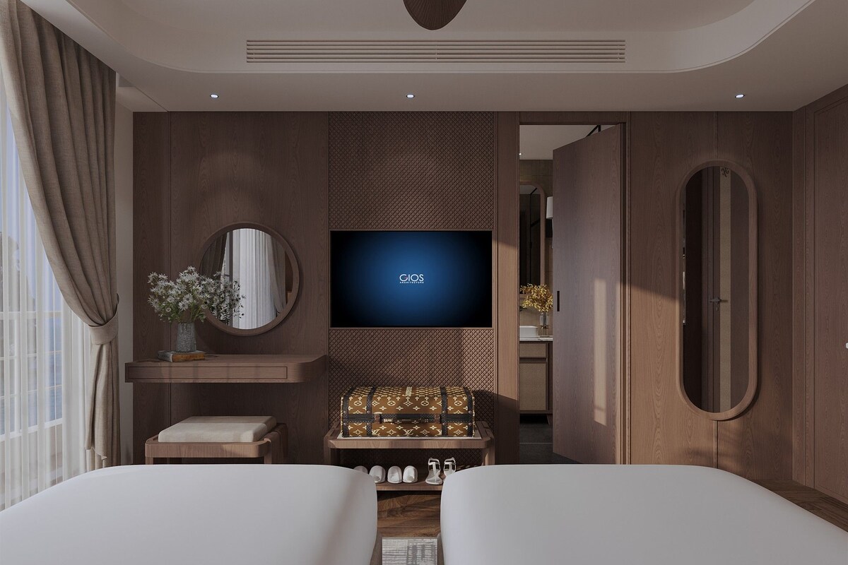 A modern hotel room with a large bed, a television, a mirror, and a small table with a Louis Vuitton bag.