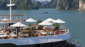 A cruise ship deck with sun loungers, umbrellas, and lifebuoys. - Harmony Boutique Cruise (Tuan Chau)