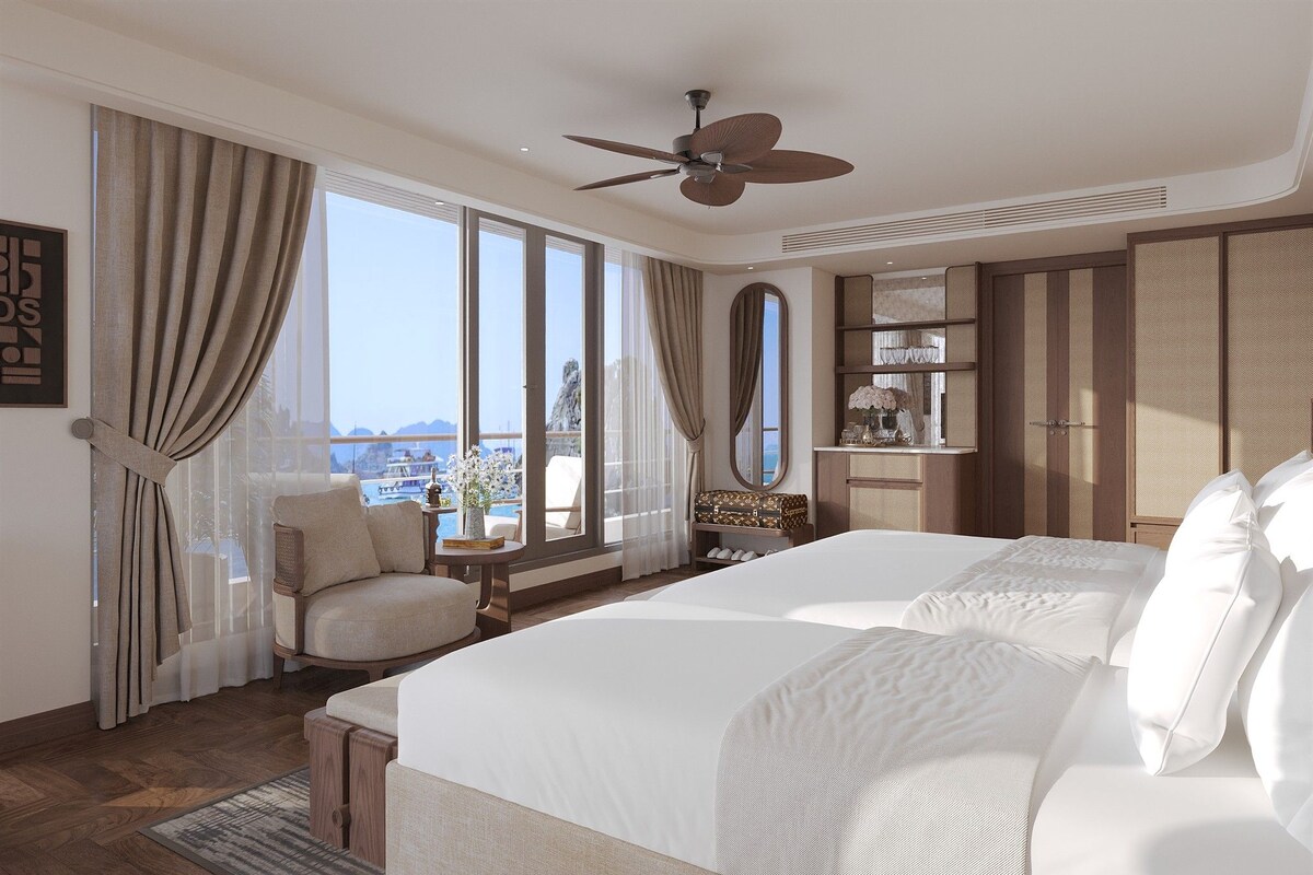 A hotel room with a large bed, a chair, a desk, and a view of the sea.