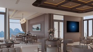 Un espace de restauration moderne, doté de plusieurs tables et chaises, d’un téléviseur fixé au mur et offrant une vue panoramique grâce à de grandes fenêtres.