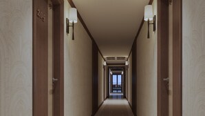 Un couloir d’hôtel avec des portes en bois, des panneaux indiquant le numéro des chambres et des lampes fixées au mur.