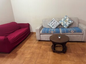 A living room with a red sofa, a grey sofa with patterned cushions, and a round wooden coffee table. - Dragonfly Pavia (Pavia)